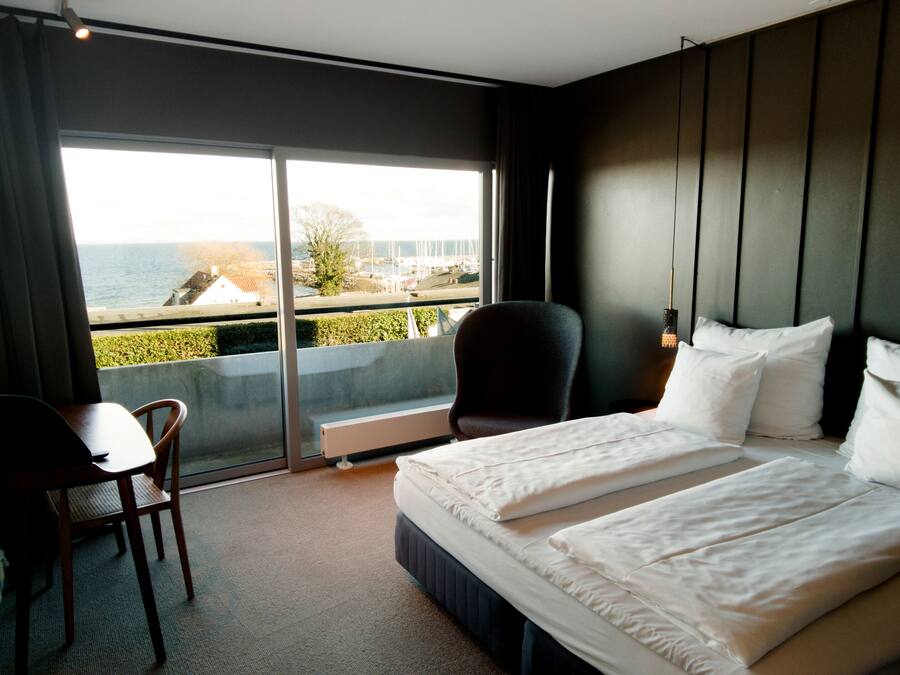 Una habitación de hotel con cama, una silla, un escritorio y un ventanal con vista al mar.
