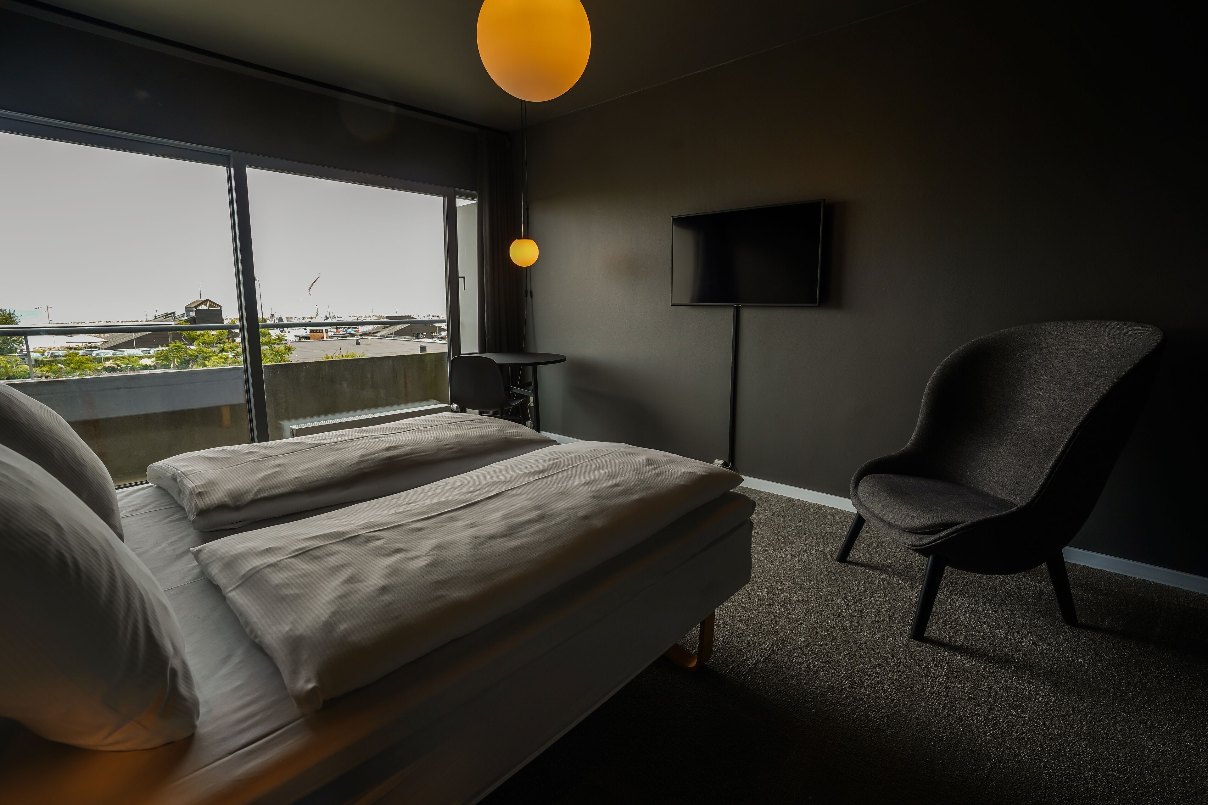 Een moderne hotelkamer met een groot bed, een fauteuil, een televisie en uitzicht op de stad.