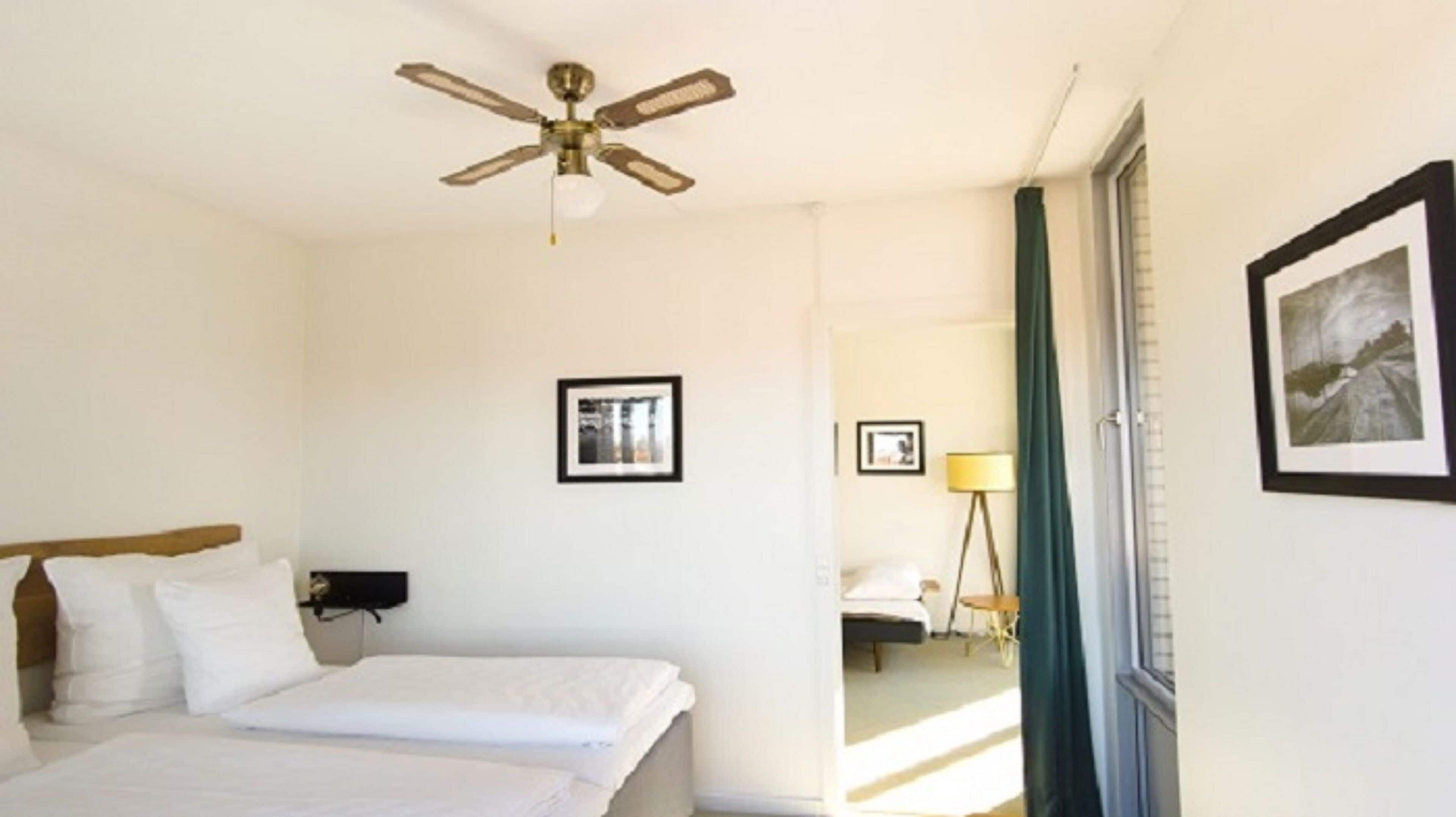 Una habitación de hotel con una cama, un ventilador de techo y cuadros en las paredes.