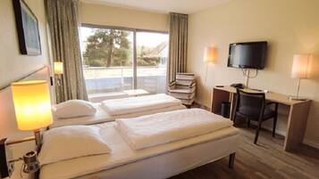 A hotel room with two beds, a desk, a chair, a television, and a window with curtains.