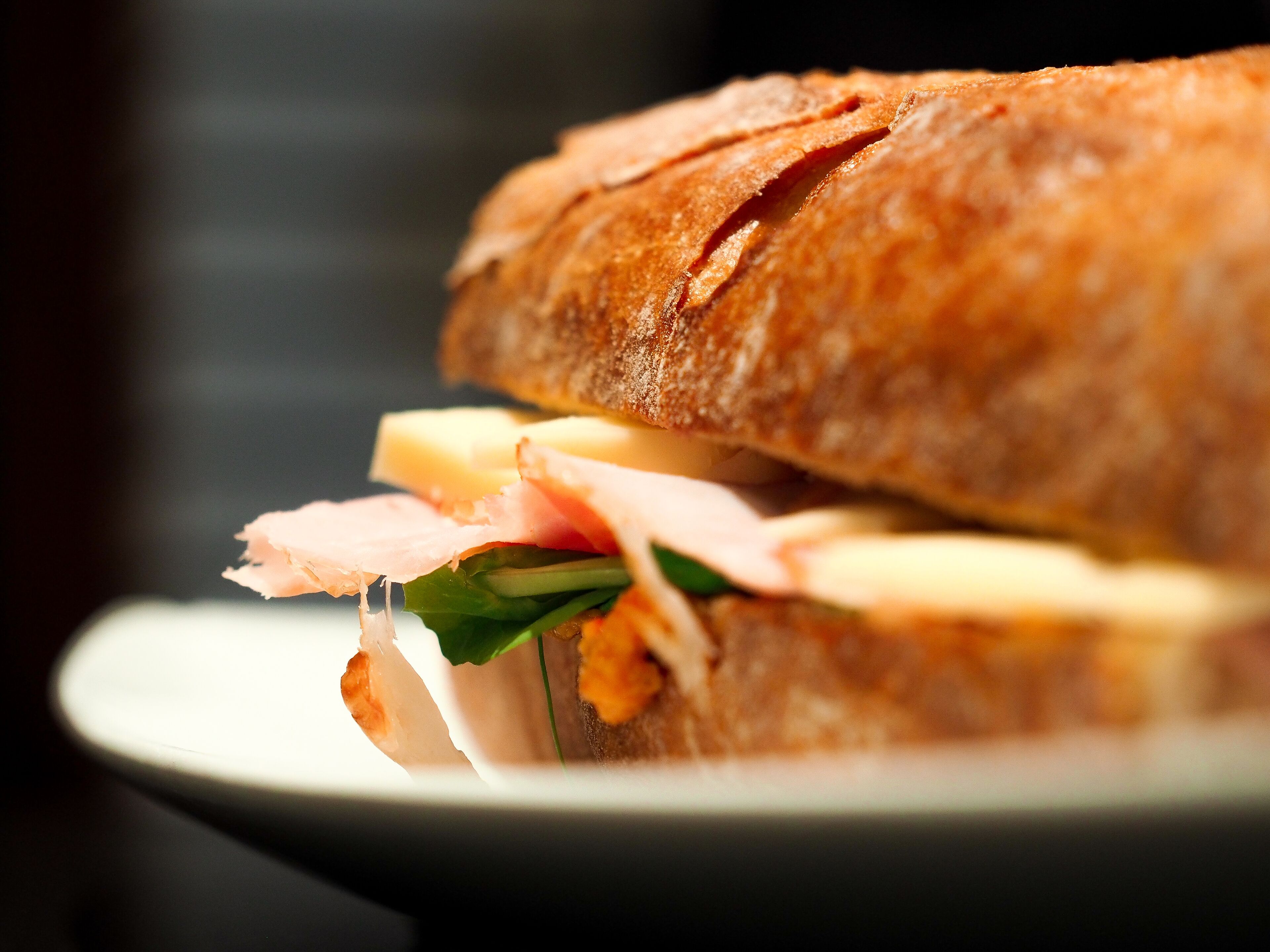 A sandwich with visible layers of ham, cheese, and greens on a plate.
