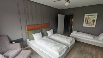 Een moderne hotelkamer met een groot bed, een kleiner bed, een zithoek en een plafondventilator.