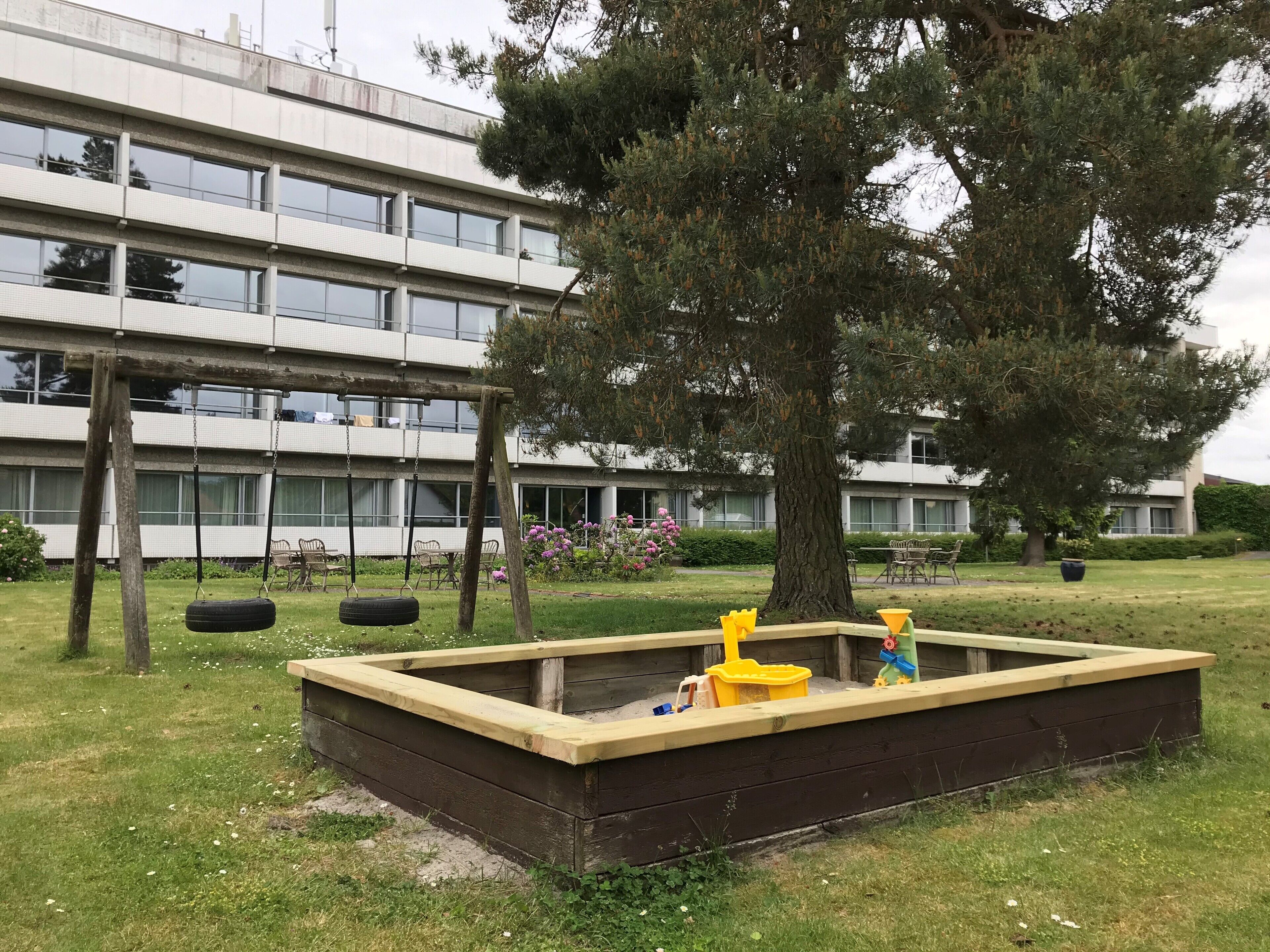 A playground with a tire swing and a sandbox in front of a modern building.