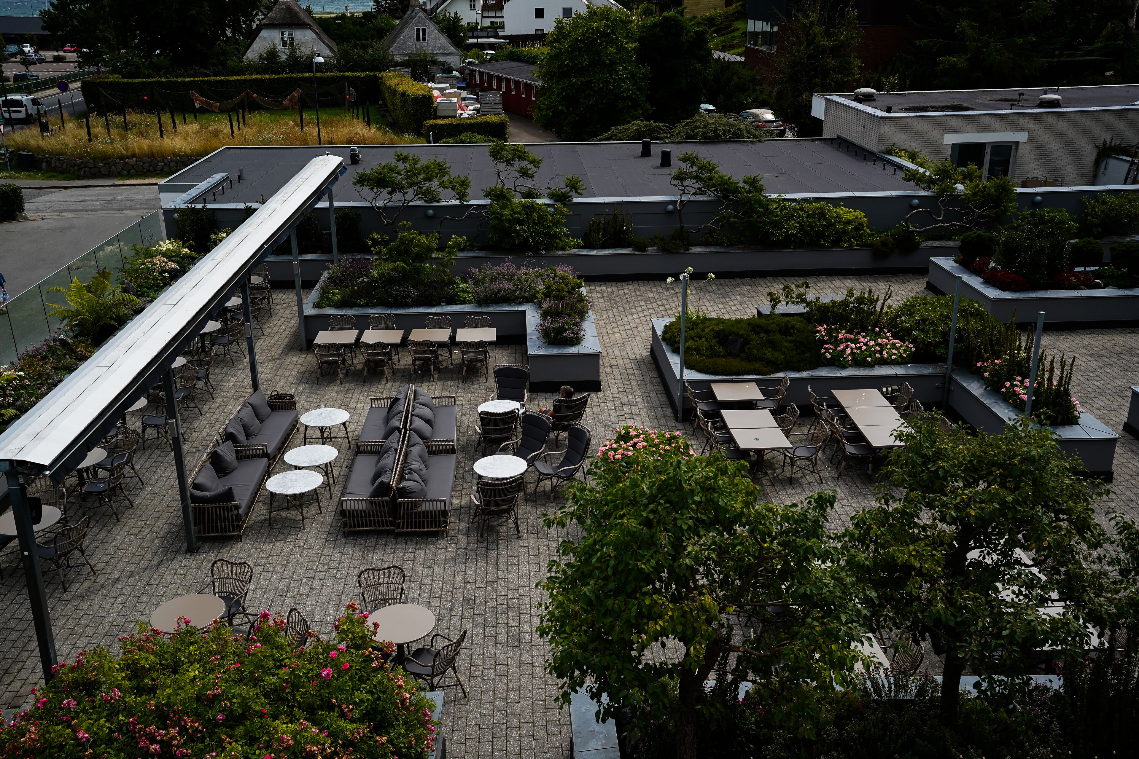 Un patio al aire libre con varias áreas de estar, incluyendo sofás y mesas, rodeado de vegetación y plantas en macetas.