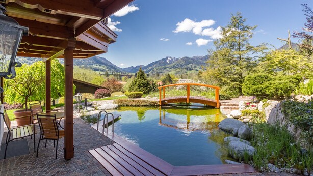 A wooden deck with outdoor seating, a small pond, and a wooden bridge. - BERGSUCHT-Ruhpolding (Ruhpolding)