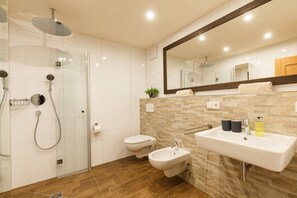 Un baño moderno con ducha de vidrio, un bidé, un lavamanos y un espejo.