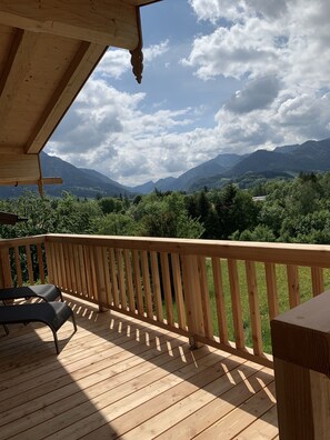 Una terraza de madera con barandilla, dos sillas y una mesa.