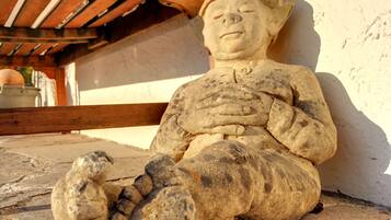 A stone statue of a seated figure with a hat, positioned against a wall with a wooden structure in the background.