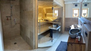 A modern bathroom with a shower, a wooden bench, and a sink with toiletries. - BERGSUCHT-Ruhpolding (Ruhpolding)
