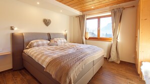 A bedroom with a wooden ceiling, a bed with a checkered bedspread, a heart-shaped wall decoration, and a window with curtains. - BERGSUCHT-Ruhpolding (Ruhpolding)