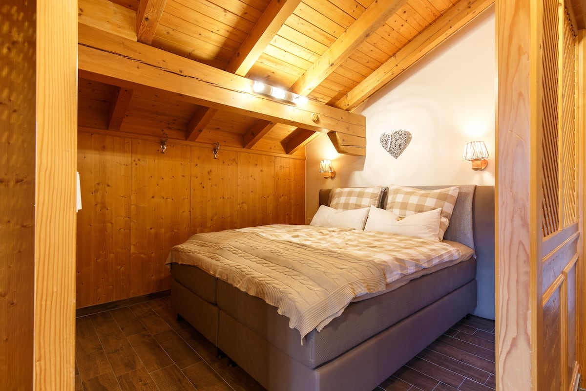 Una habitación con paneles de madera, una cama, vigas de madera y luces fijadas a la pared.