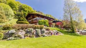 A traditional chalet with a wooden exterior, a balcony, and a well-maintained garden with various plants and a rock formation. - BERGSUCHT-Ruhpolding (Ruhpolding)