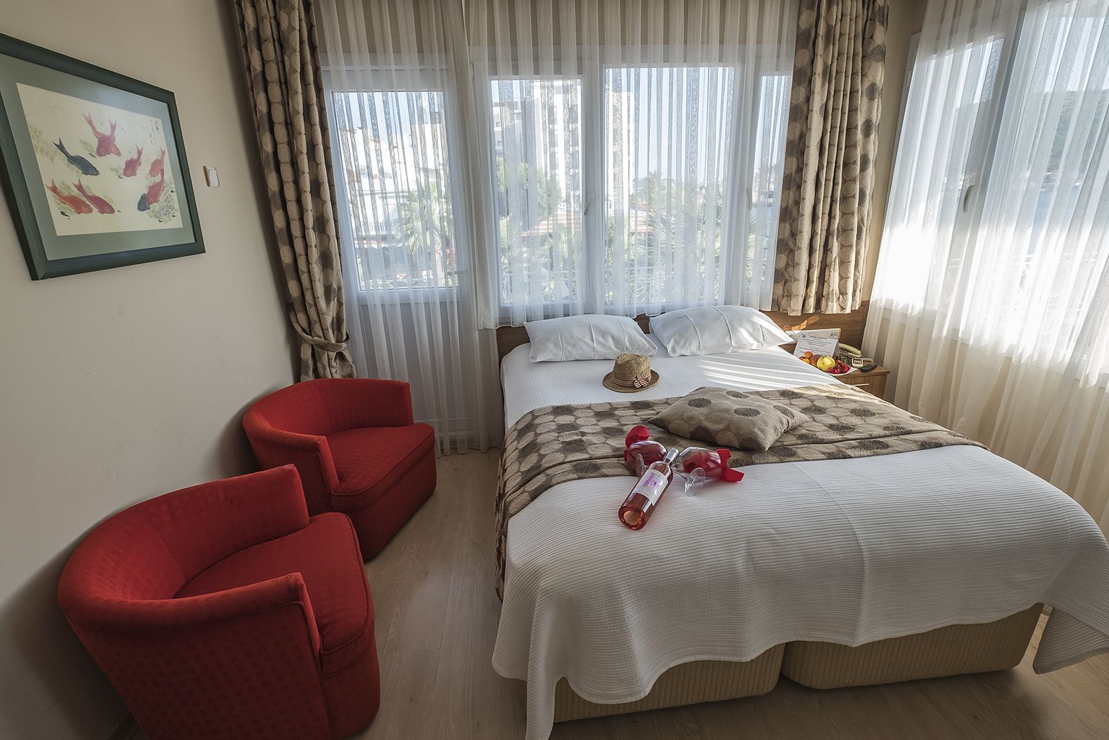 A hotel room with a bed, two red chairs, a framed picture on the wall, and a window with curtains.