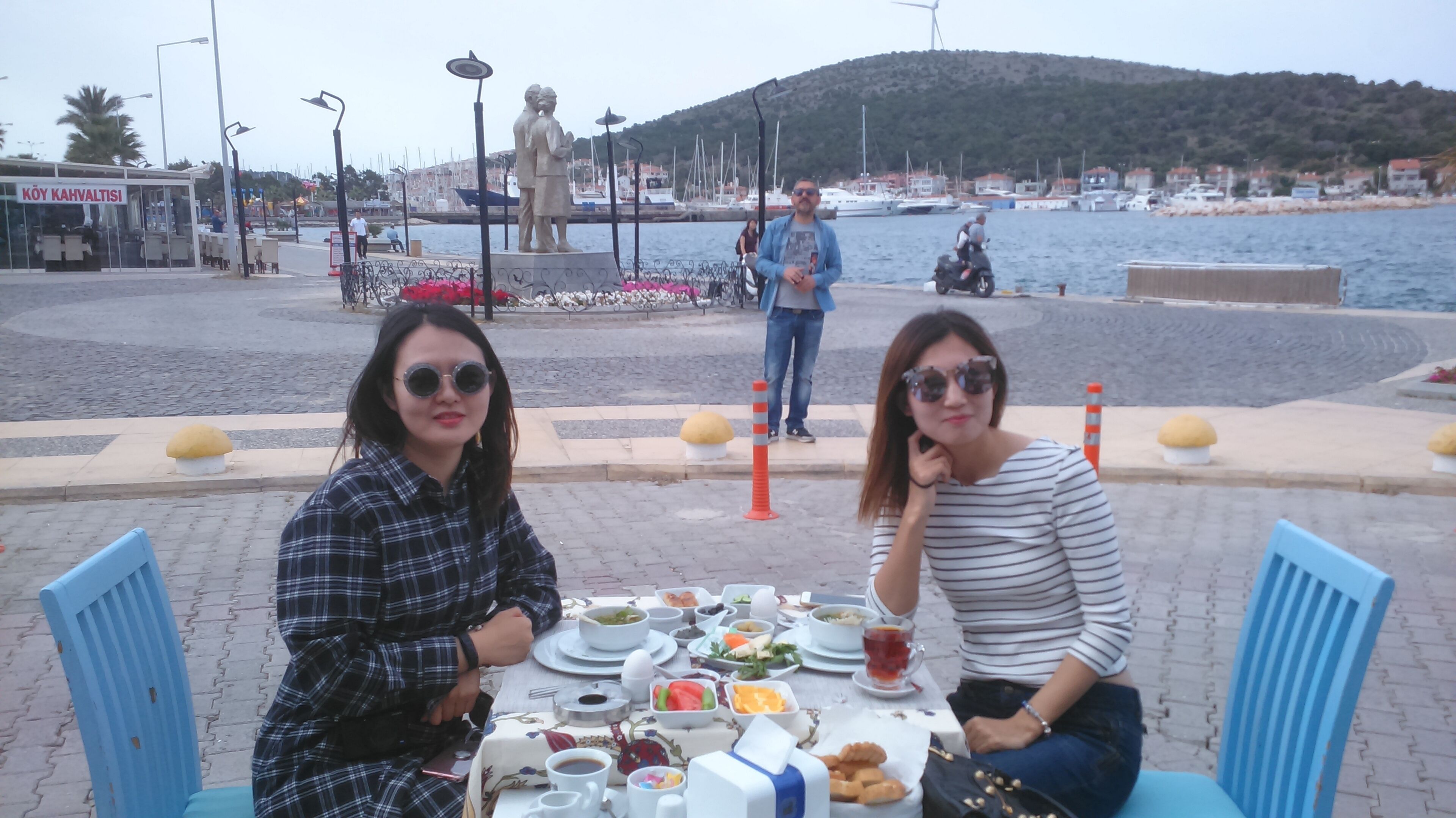 Two people dining at an outdoor table with a view of the sea and a statue in the background.