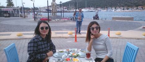 Two people dining at an outdoor table with a view of the sea and a statue in the background.