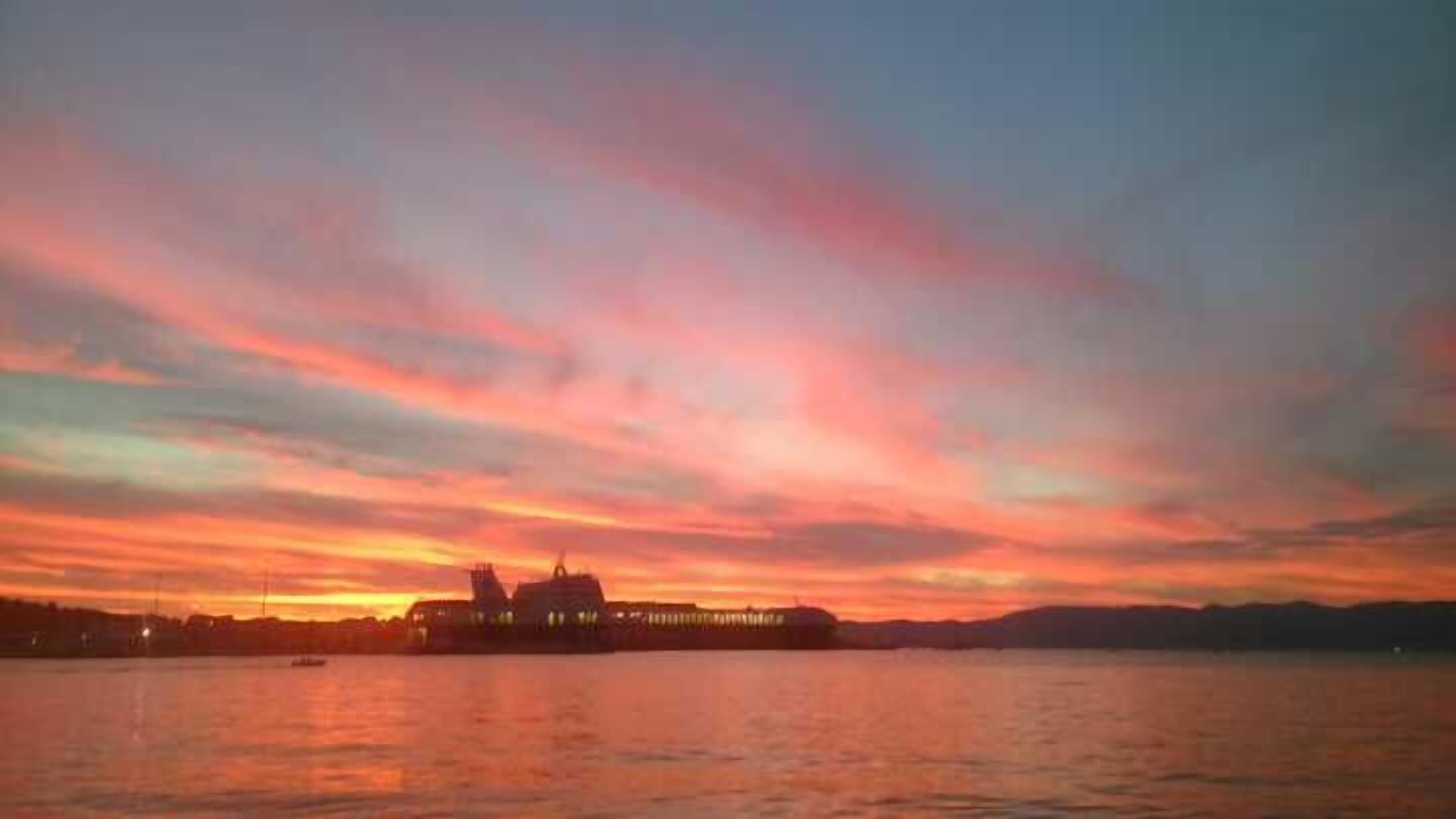 Un atardecer sobre una masa de agua, con la silueta de un edificio.