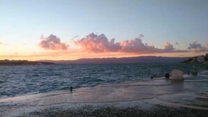 Vista al agua con atardecer, mar tranquilo y montañas a lo lejos.