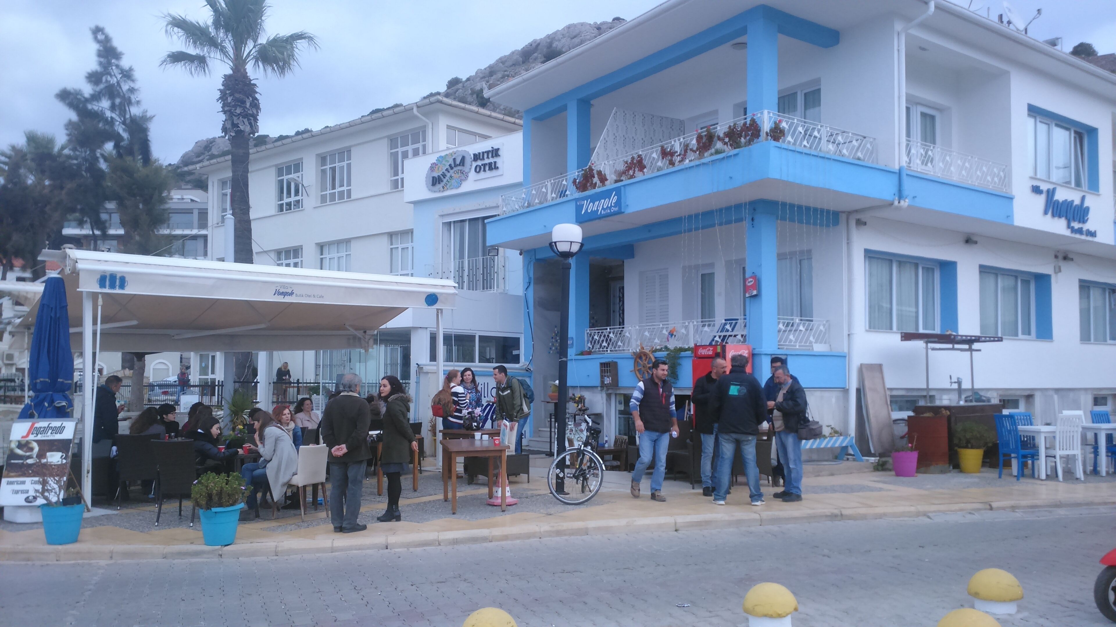 A coastal building with a blue and white facade, outdoor seating area, and a visible Coca-Cola vending machine.