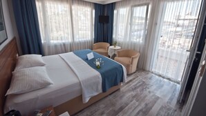 Una habitación de hotel con una cama grande, un sofá pequeño, una mesa redonda y un televisor colocado en la pared.