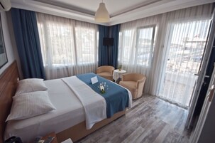 Una habitación de hotel con una cama grande, un sofá pequeño, una mesa redonda y un televisor colocado en la pared.
