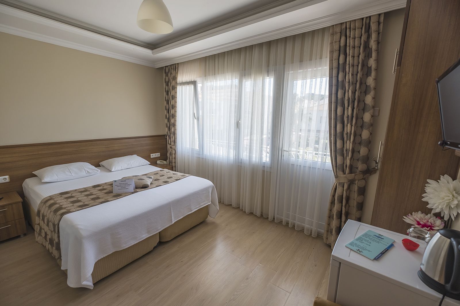 Habitación de hotel con cama, escritorio con hervidor y vistas al exterior a través de cortinas translúcidas.