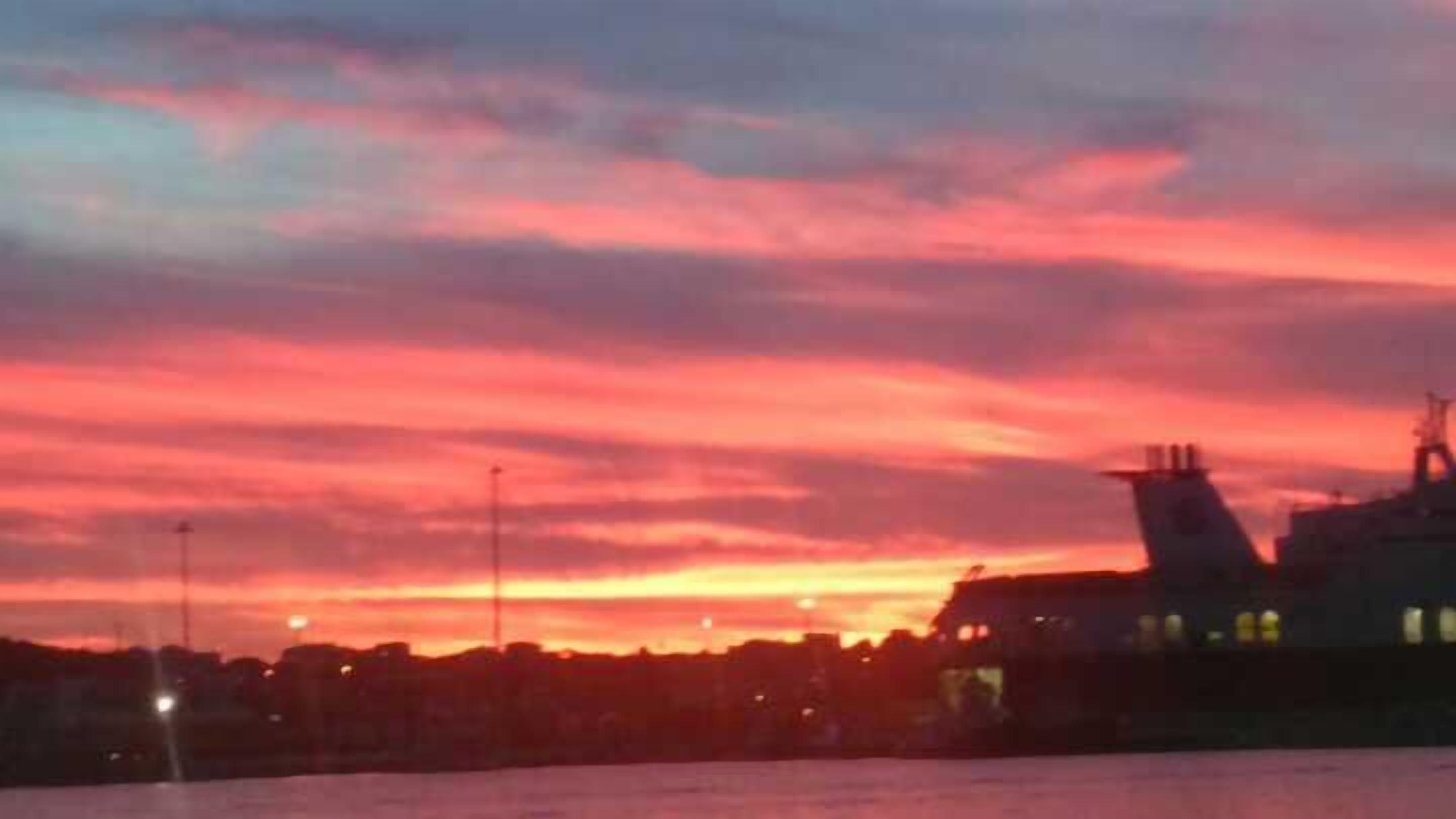 Een zonsondergang boven een stadshemel, waarbij gebouwen als silhouetten tegen de lucht staan afgebeeld.