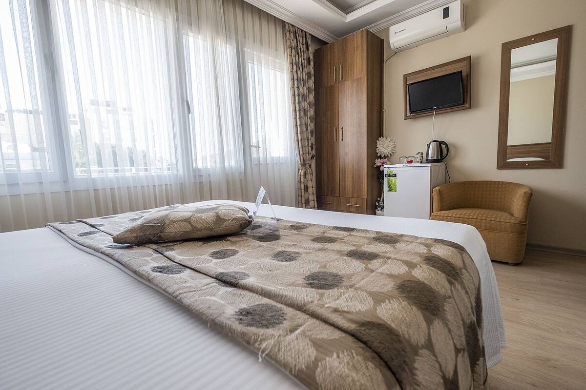 Hotellihuone, jossa on sänky, tuoli, työpöytä, televisio ja peili.