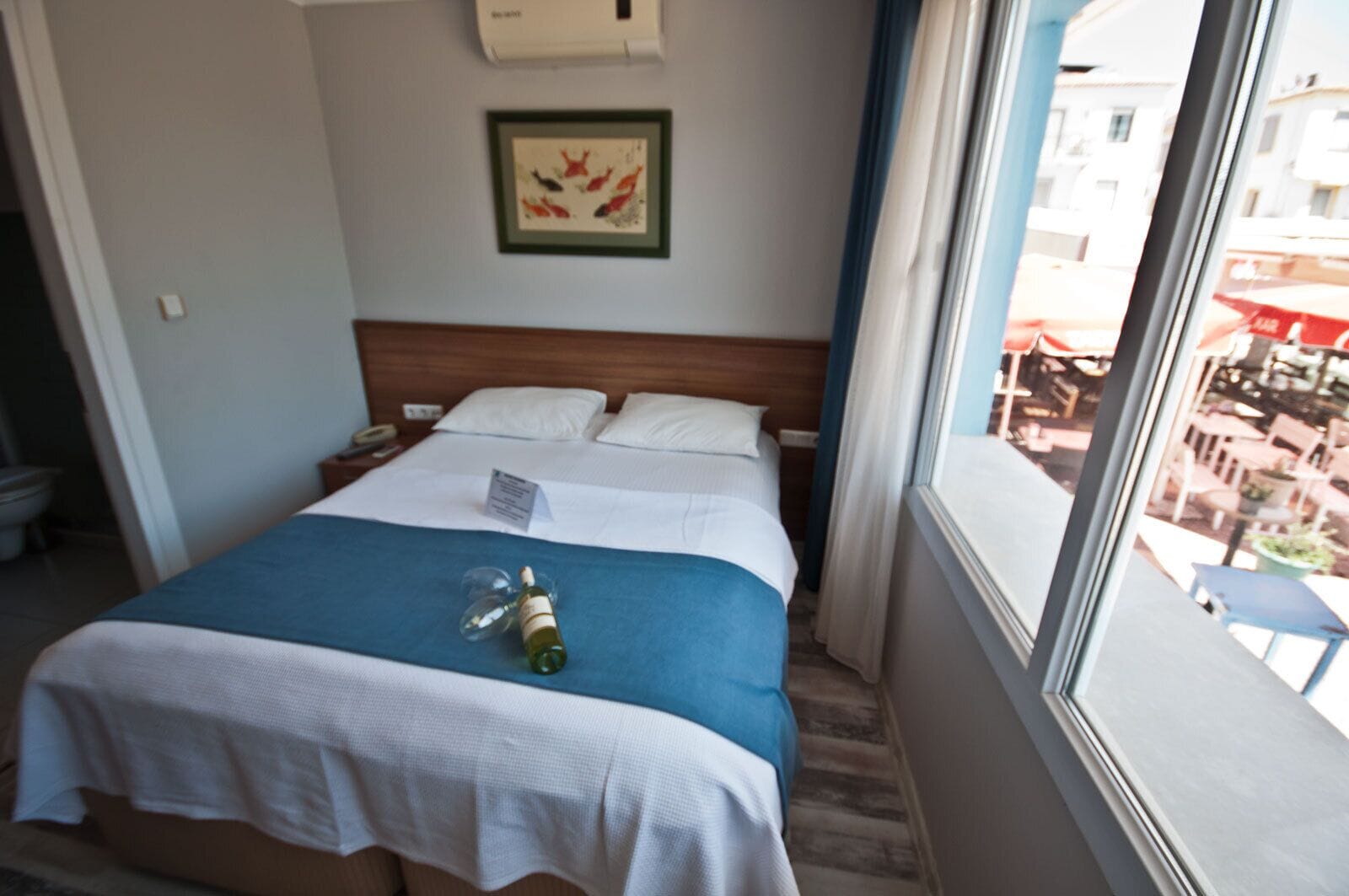 Una habitación de hotel con una cama, un ventanal con vistas al exterior y un cuadro enmarcado en la pared.