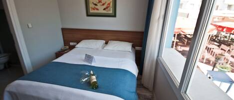 Una habitación de hotel con una cama, un ventanal con vistas al exterior y un cuadro enmarcado en la pared.