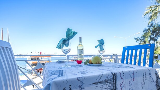 Una mesa dispuesta con una botella, copas y fruta, con vistas a un puerto deportivo lleno de barcos.