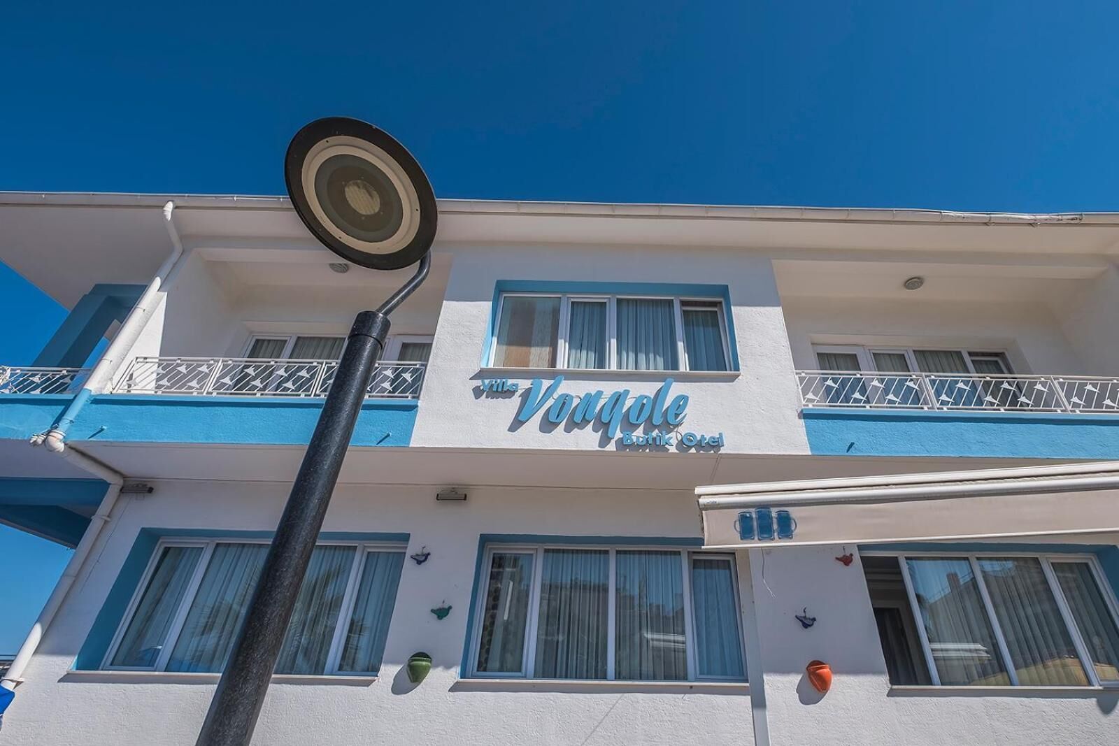 Un hotel llamado "Vogue Boutique Hotel" con fachada blanca y azul, numerosas ventanas y un balcón con barandillas blancas.