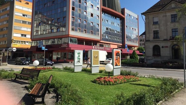 A modern building with a glass facade, a restaurant, and a sign for 'Art Prime'. - Hôtel des Trois Rois (Le Locle)