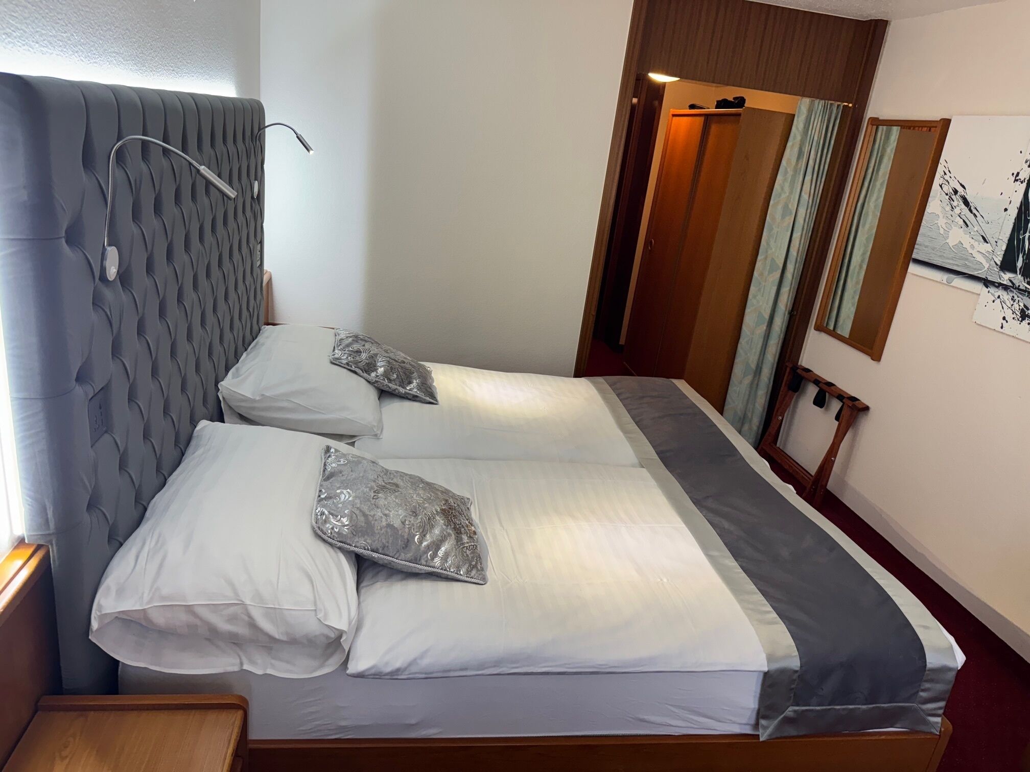 A neatly made bed with white and gray linens, a headboard with a textured pattern, and a wooden nightstand.