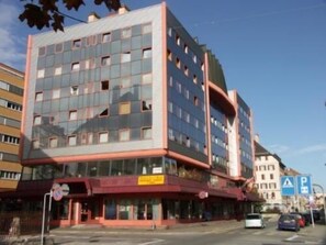 A multi-story hotel with a modern architectural design, featuring a mix of glass and metal facade, and a ground-level commercial space. - Hôtel des Trois Rois (Le Locle)