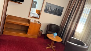 A hotel room with a wooden desk, a chair, a small round table with a globe, a television, a mirror, and a cityscape painting. - Hôtel des Trois Rois (Le Locle)