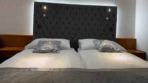 A double bed with a tufted headboard, two bedside tables, and a wall-mounted light fixture. - Hôtel des Trois Rois (Le Locle)