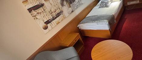 A compact room with a bed, a grey sofa, a small wooden table, and a large abstract painting on the wall.