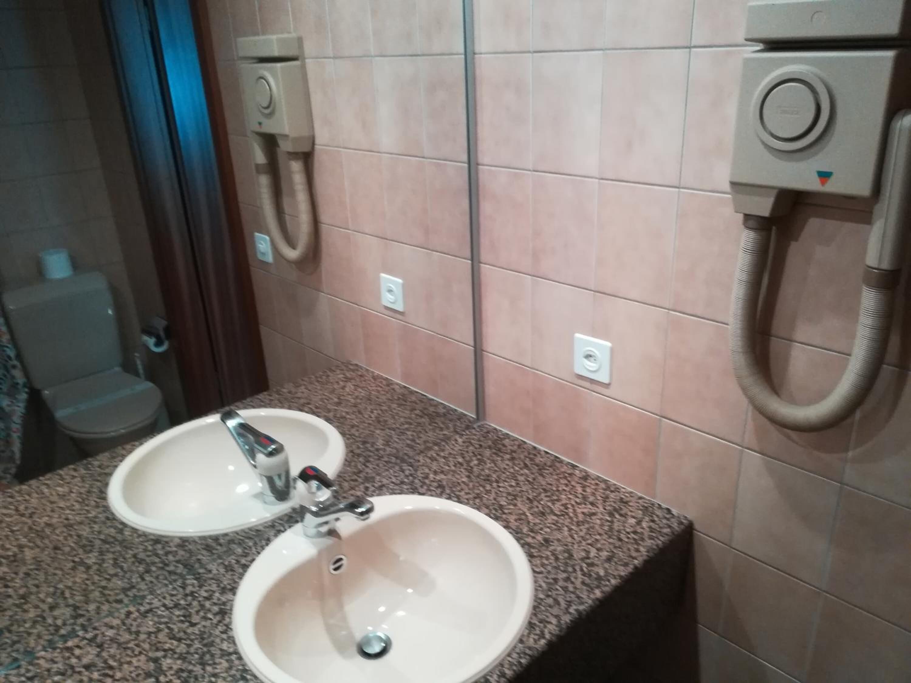 A bathroom with two sinks, a mirror, and a toilet.