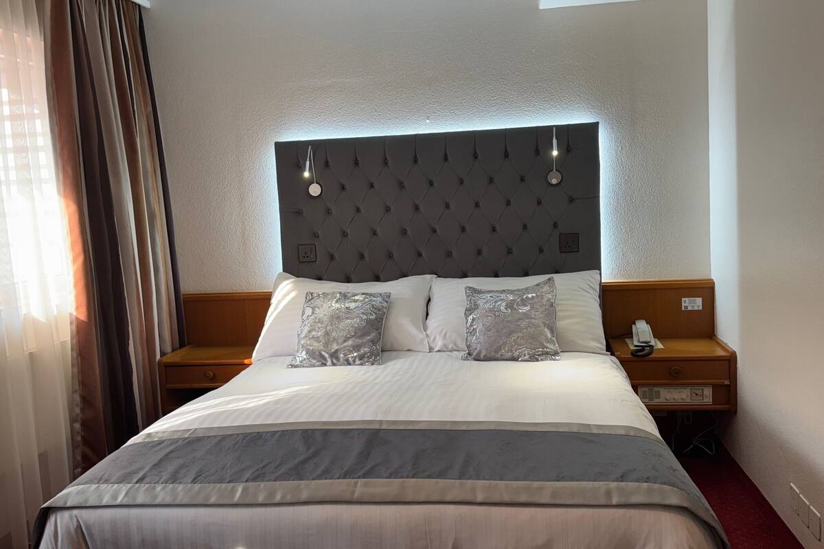 A hotel room with a large bed, a headboard with lights, two bedside tables, and a telephone.