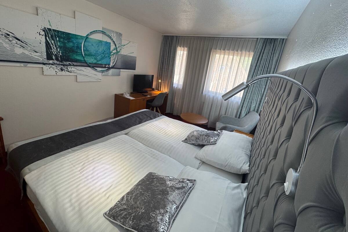 A hotel room with a large bed, a desk with a computer, a TV, and a window with curtains.