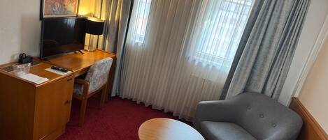 A hotel room with a desk, chair, and a small round table.