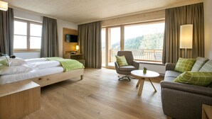 A hotel room with a bed, a sofa, a chair, a small table, and a TV.