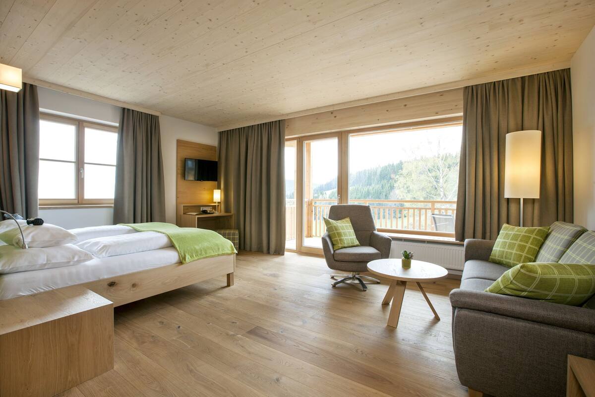 Ein Hotelzimmer mit Bett, einer Sitzecke, einem Sessel, einem kleinen Tisch und einem Fernseher.