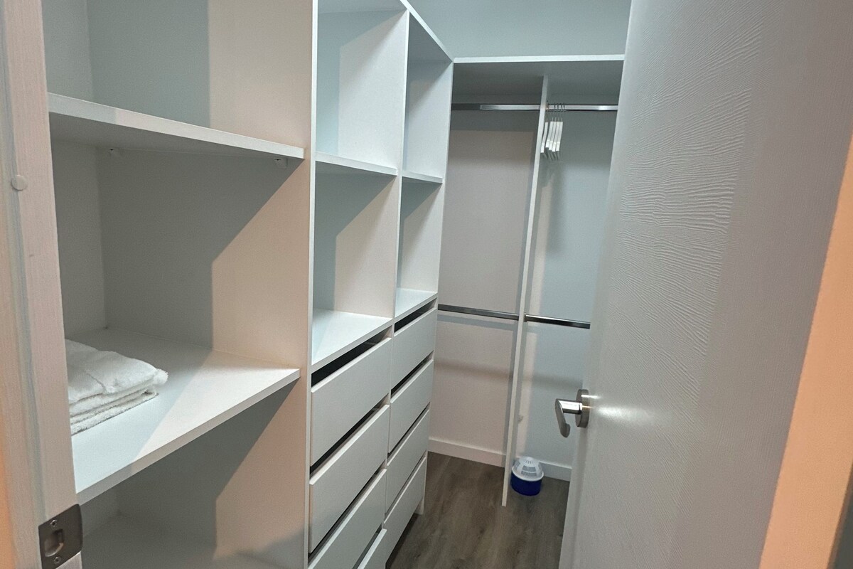 Um closet espaçoso com prateleiras abertas, cabideiro e porta com puxador.