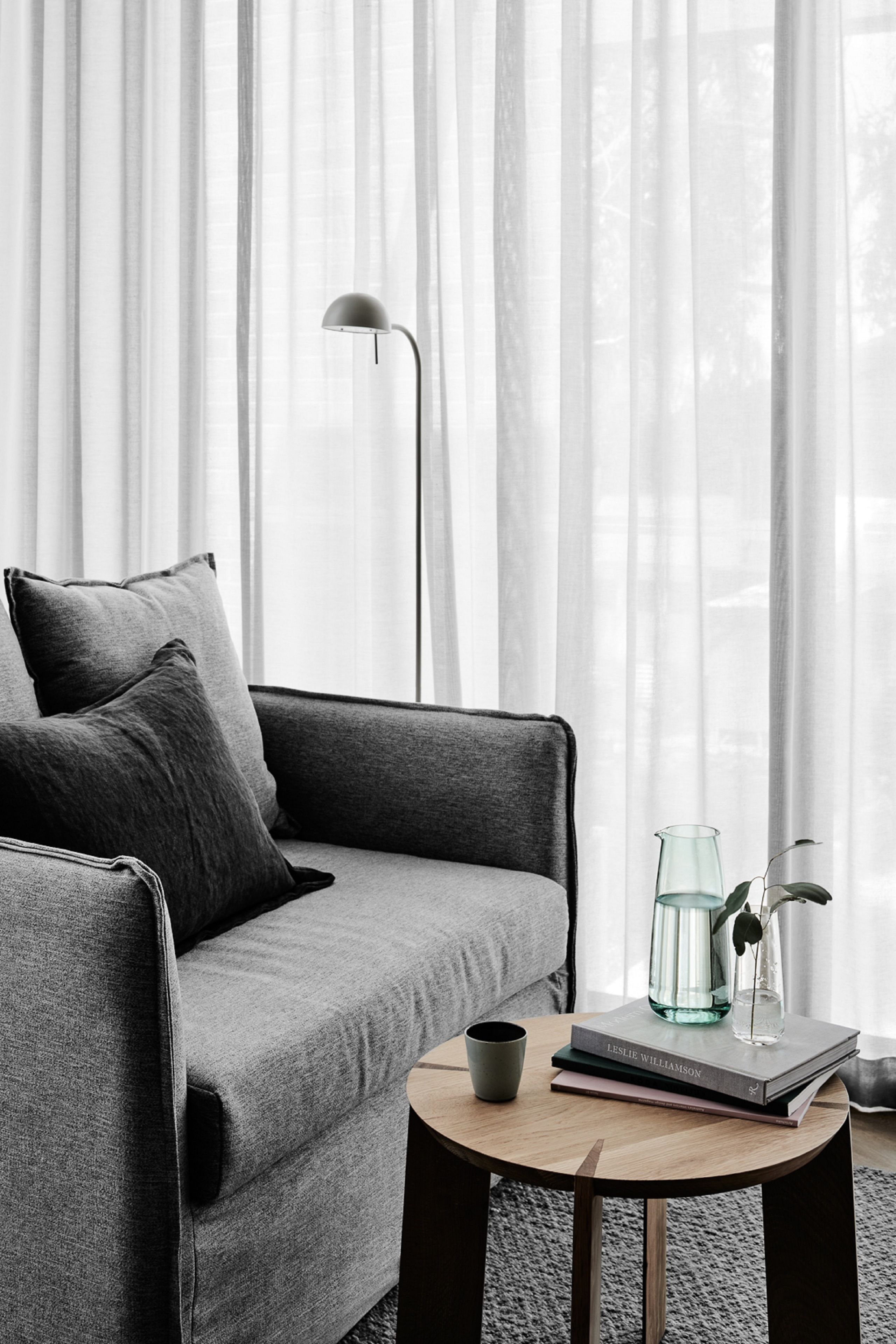 A modern living room with a grey sofa, a round wooden coffee table, and a floor lamp.