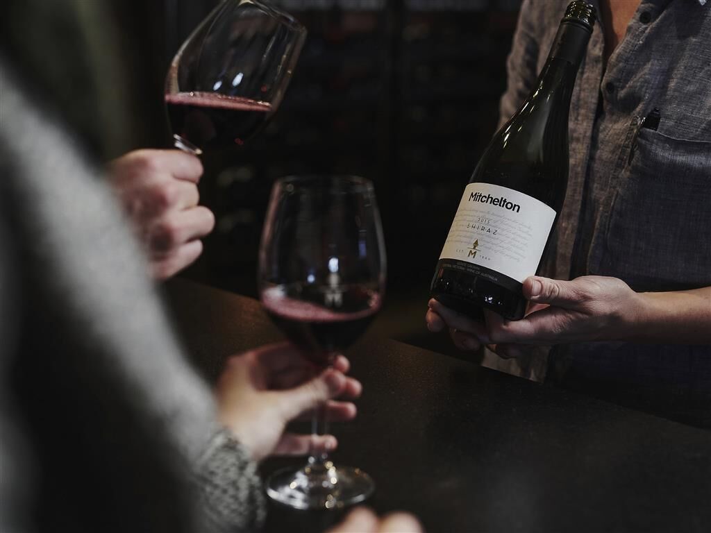 A person holding a wine bottle labeled 'Mitchelton' with a wine glass in the foreground.