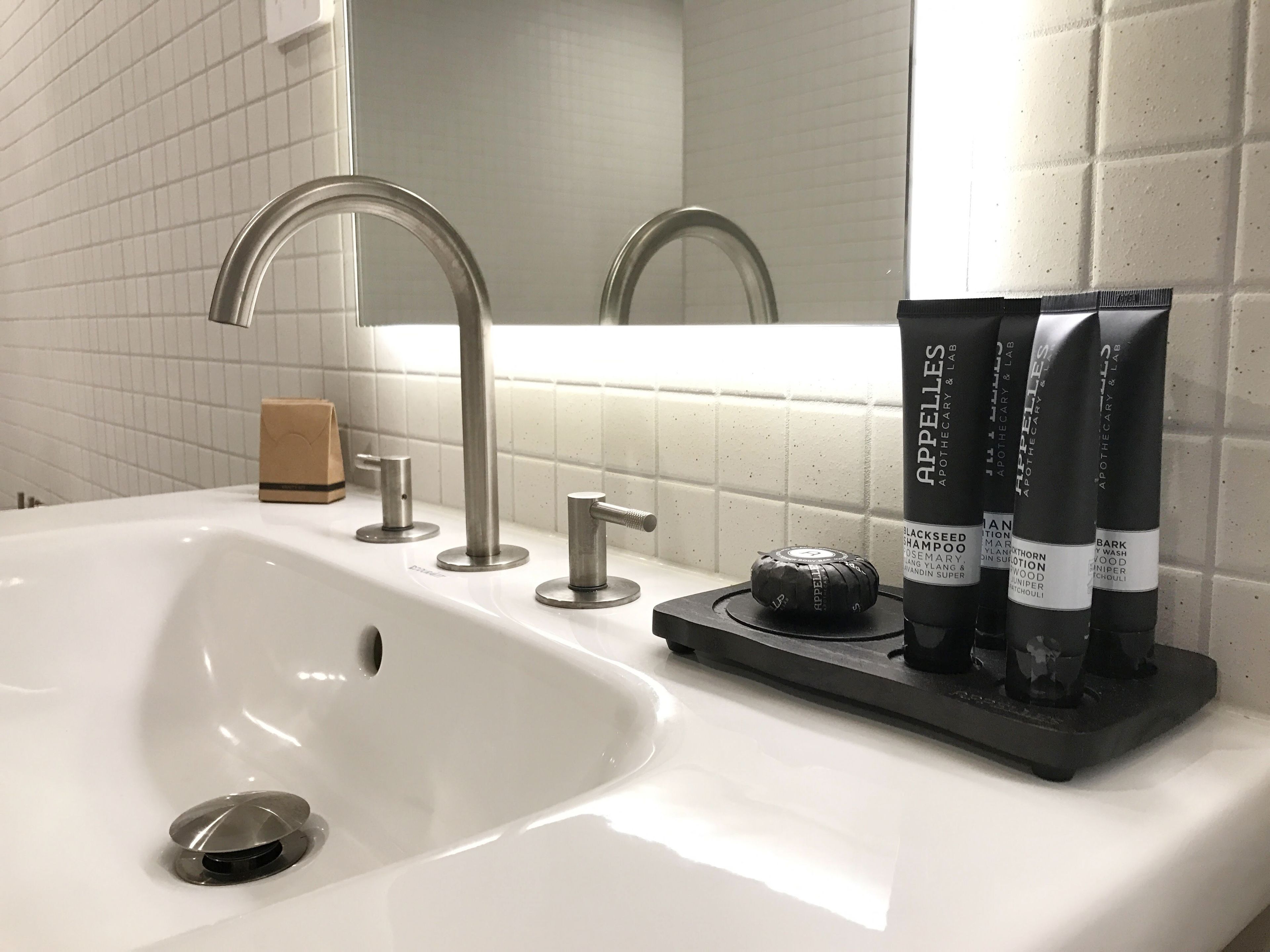 Un lavabo de salle de bain avec un robinet moderne, un distributeur de savon et trois bouteilles de shampoing à base de graines noires.