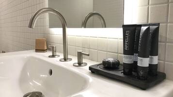 Un lavabo de salle de bain avec un robinet moderne, un distributeur de savon et trois bouteilles de shampoing à base de graines noires.