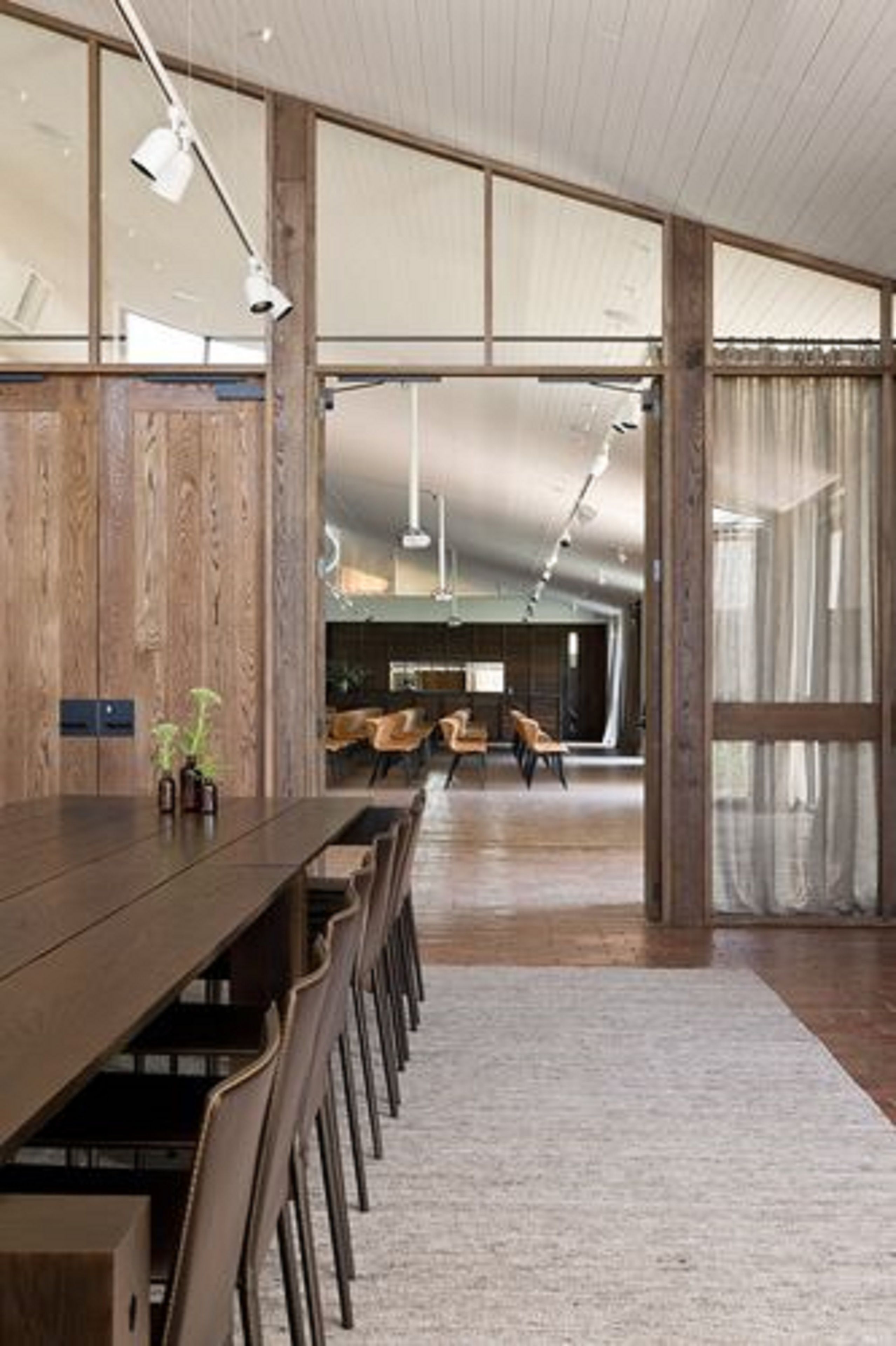 Une pièce spacieuse avec une longue table en bois et des chaises, de grandes fenêtres et un plafond haut.