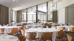 Un vaste espace dédié à la salle à manger, avec des tables rondes, des chaises en osier et de grandes fenêtres laissant entrer la lumière naturelle.